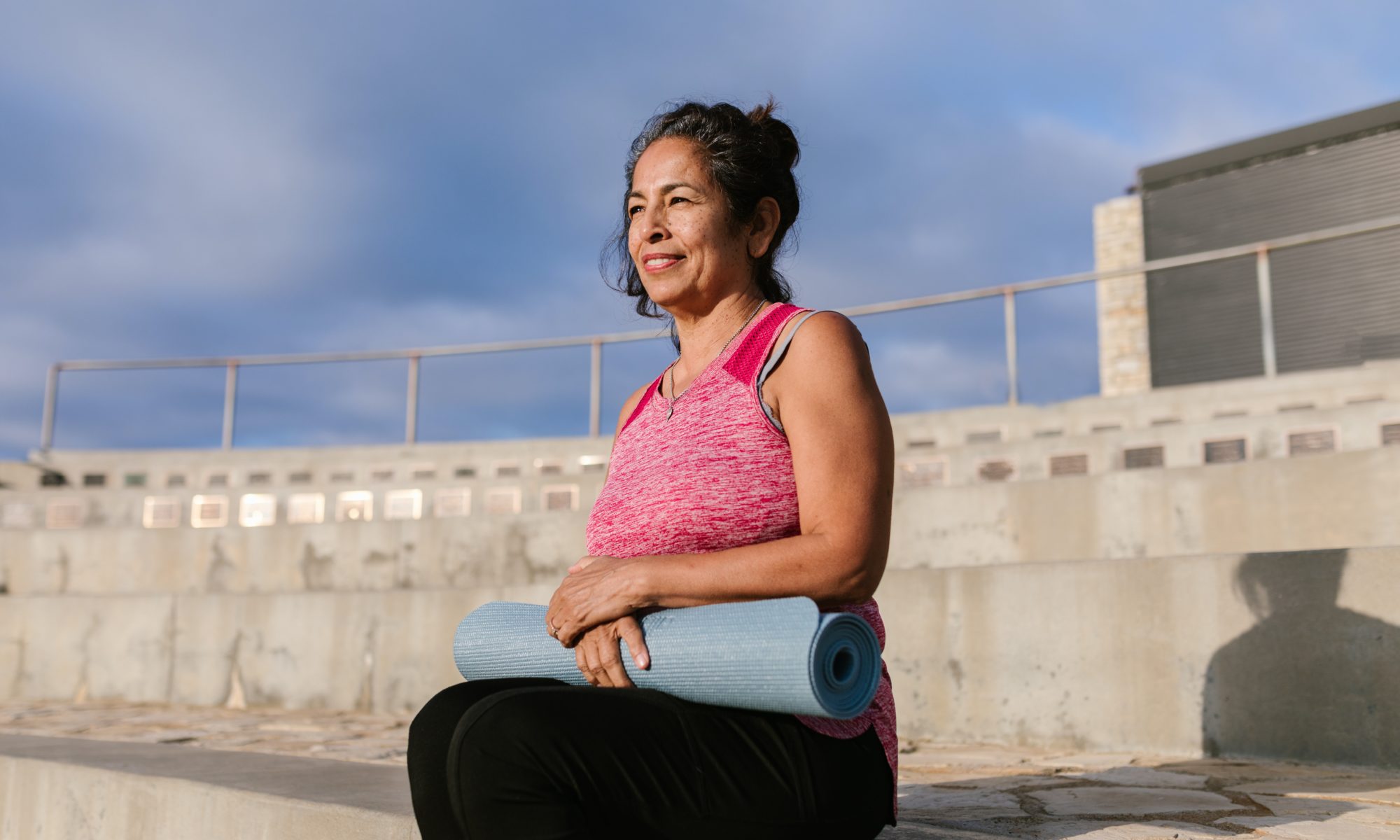 Smiling woman sitting and holding a yoga mat.